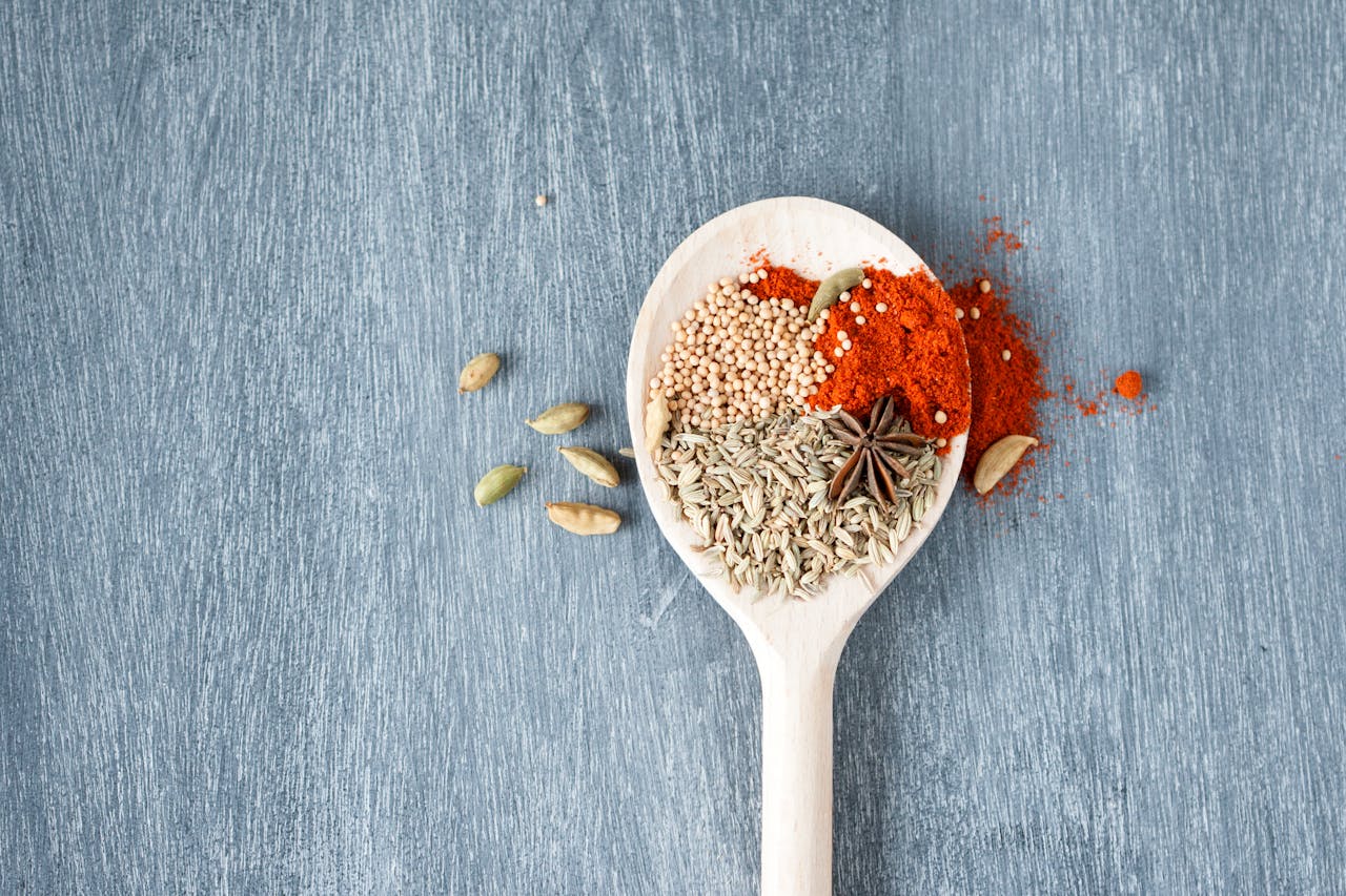 who-we-are A collection of vibrant spices displayed on a wooden spoon against a textured background.