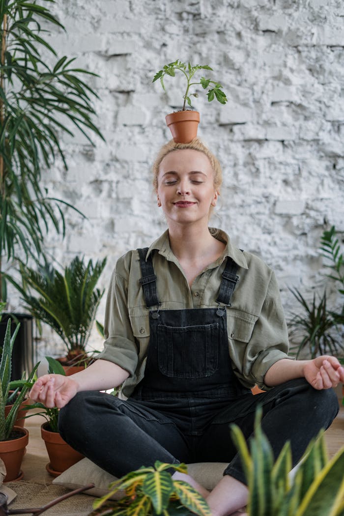 team-04 Woman meditating indoors surrounded by potted plants, balancing a pot on her head.