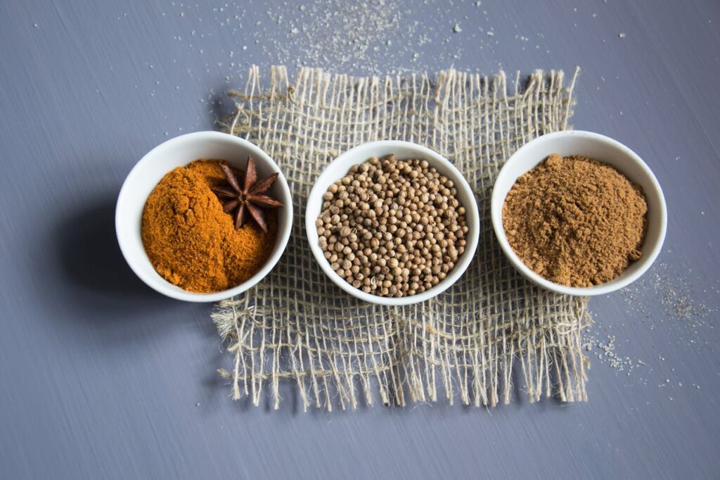 Flat lay of aromatic spices in bowls on a textured mat.